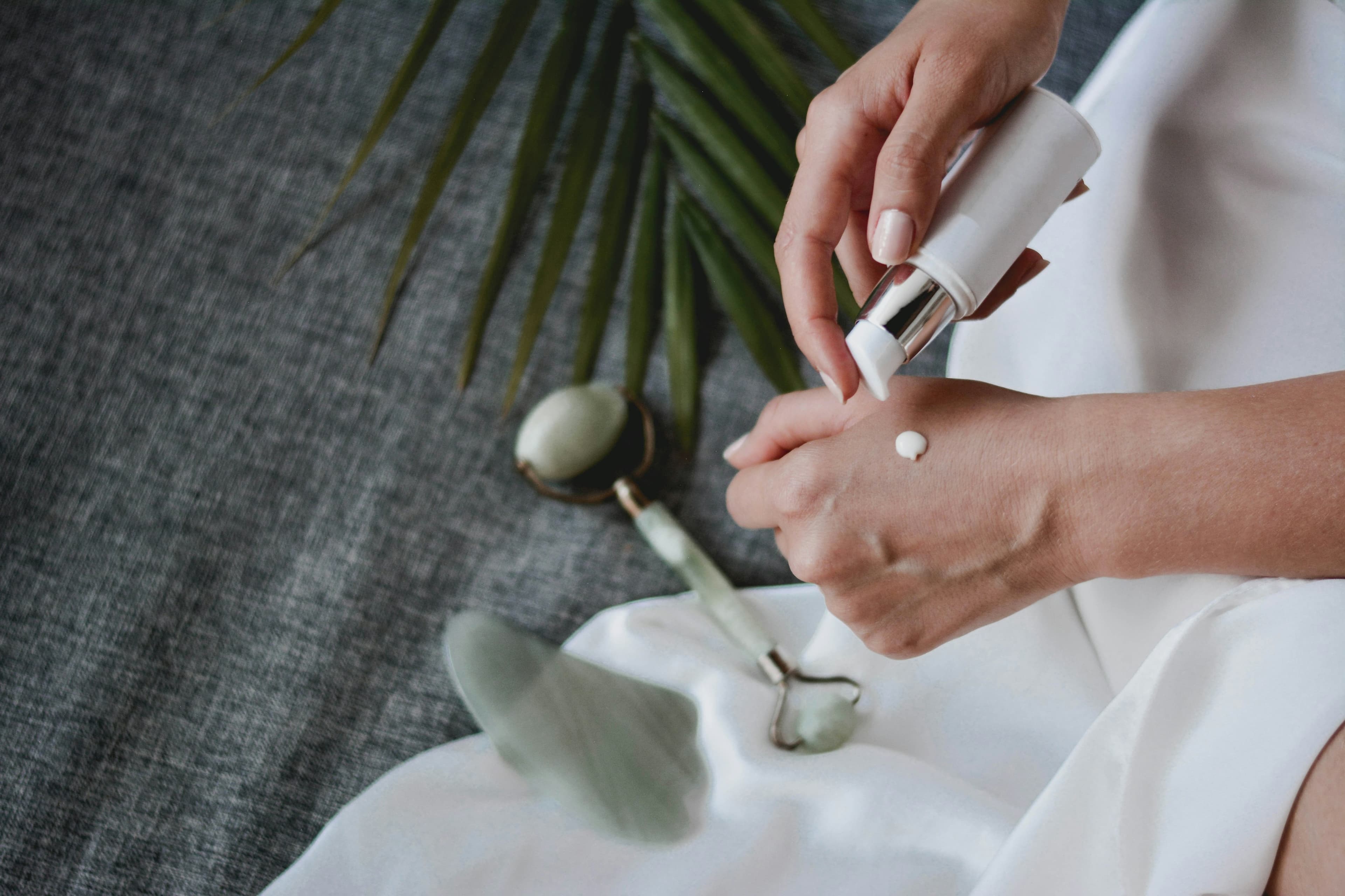 Hands applying cream beside a jade roller